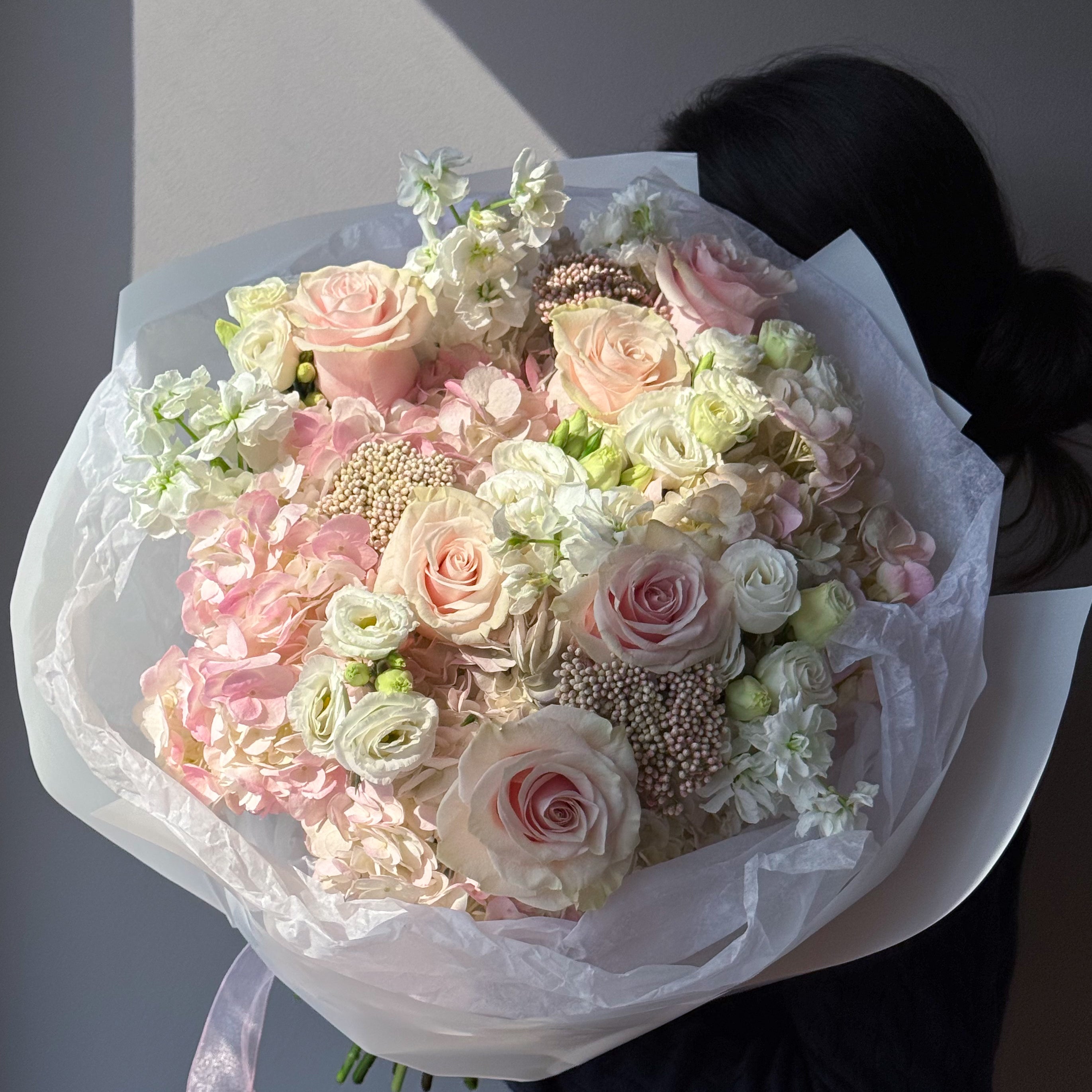 Large pastel bouquet with blush roses, white hydrangeas, and soft pink flowers wrapped in white paper