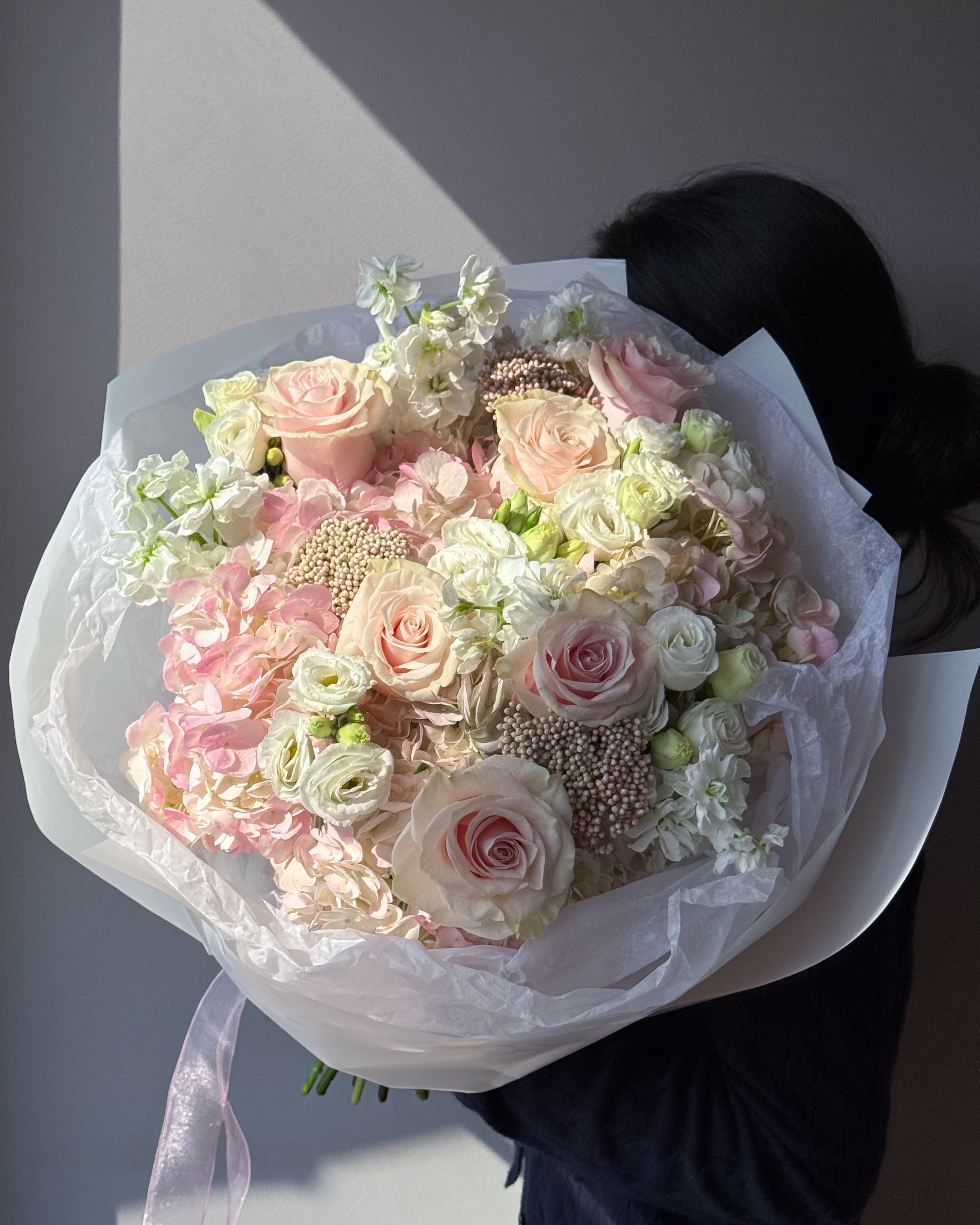 Large pastel bouquet with blush roses, white hydrangeas, and soft pink flowers wrapped in white paper