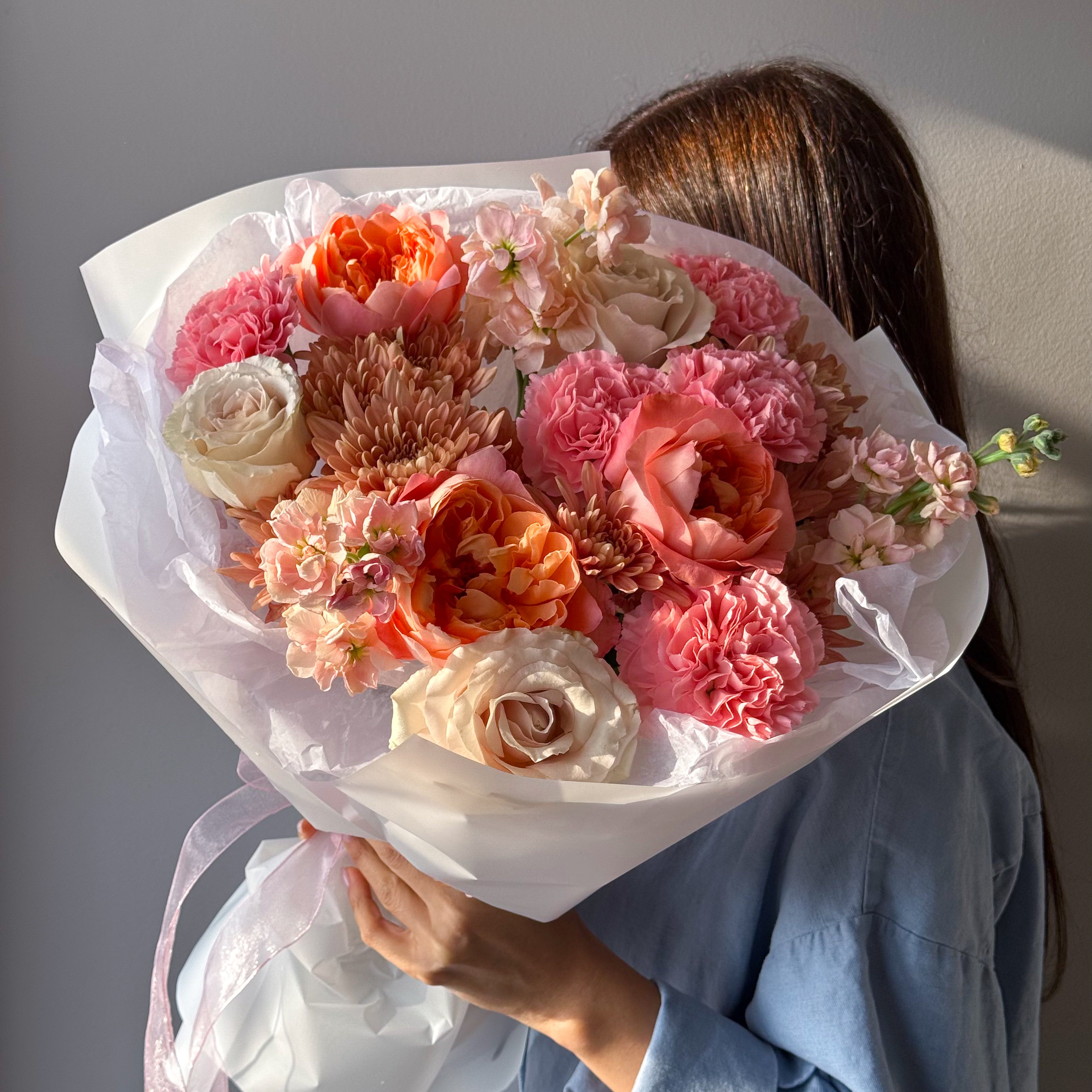 Close-up of “Sunset Glow” bouquet highlighting peach roses, coral blooms, and soft blush tones.