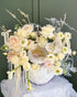 Luxury ivory and champagne floral arrangement featuring roses, orchids, and seasonal blooms in a decorative white pumpkin with pearl and gold accents.