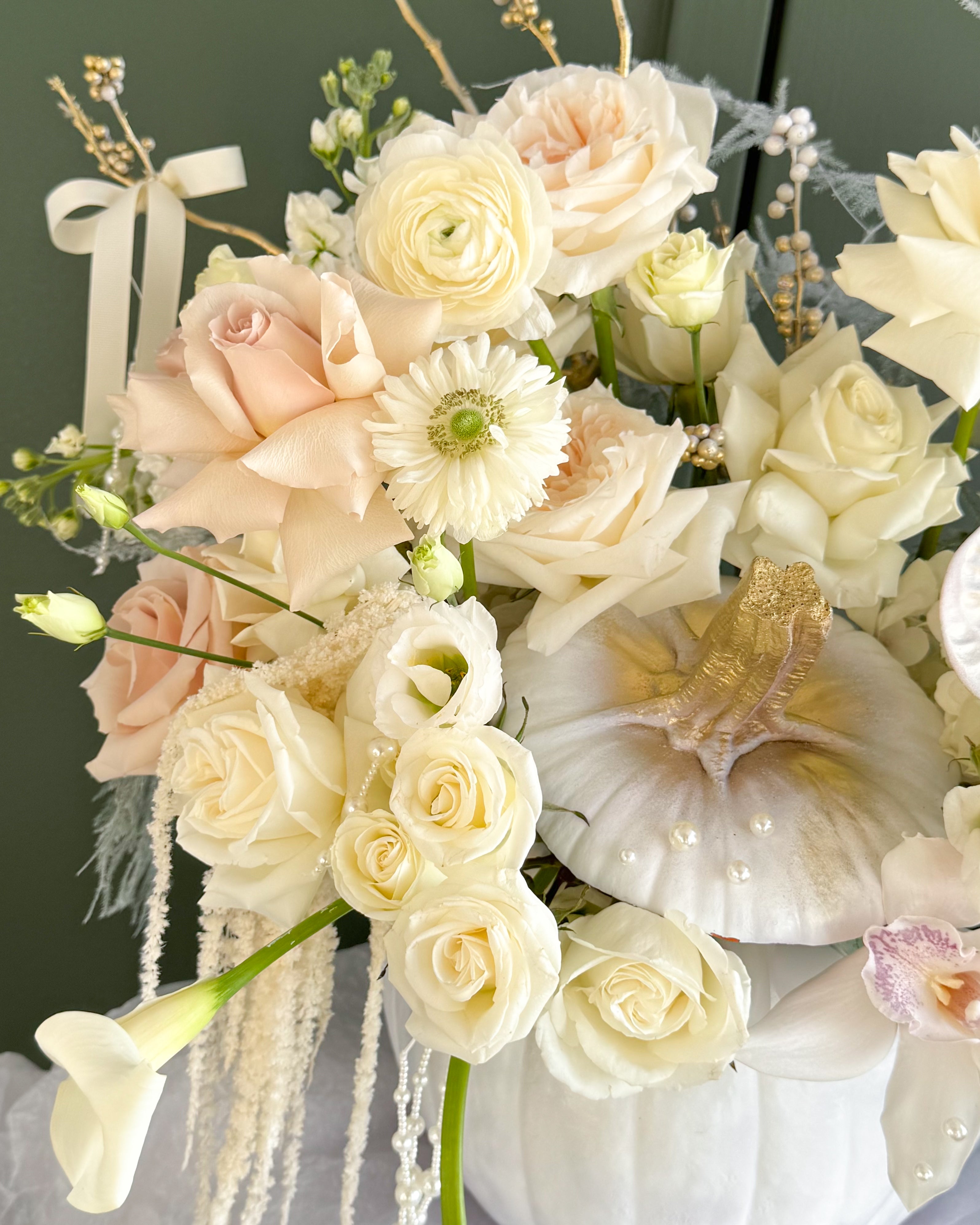 Luxury ivory and champagne floral arrangement featuring roses, orchids, and seasonal blooms in a decorative white pumpkin with pearl and gold accents.