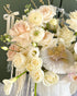 Luxury ivory and champagne floral arrangement featuring roses, orchids, and seasonal blooms in a decorative white pumpkin with pearl and gold accents.